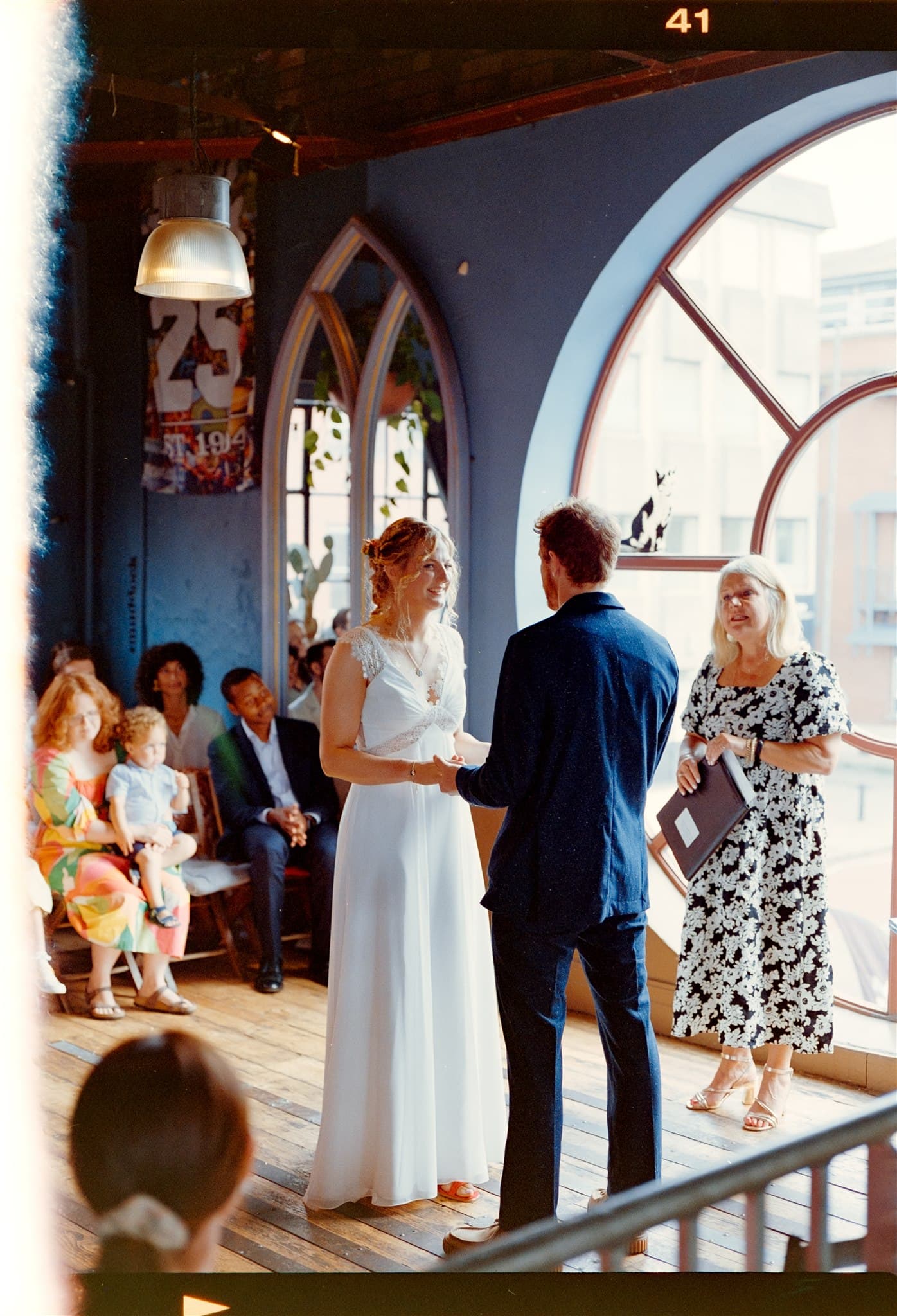 A couple holding hands at their wedding ceremony with guests seated on the side.