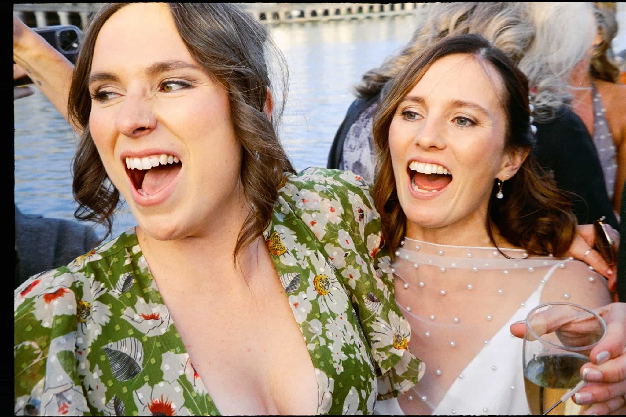 Two women share a smile and raise their wine glasses in a heartfelt toast, beautifully captured in a film photo.