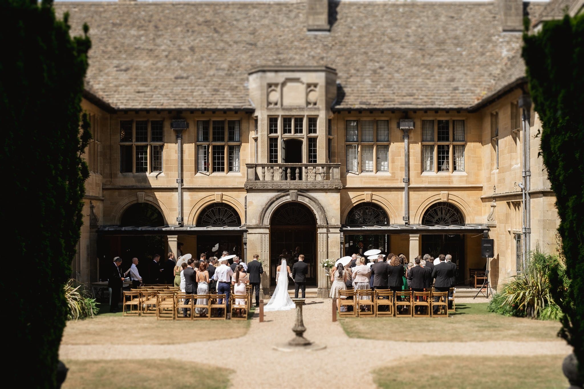 Outdoor wedding ceremony at a historic building, guests gathered around the bridal couple.