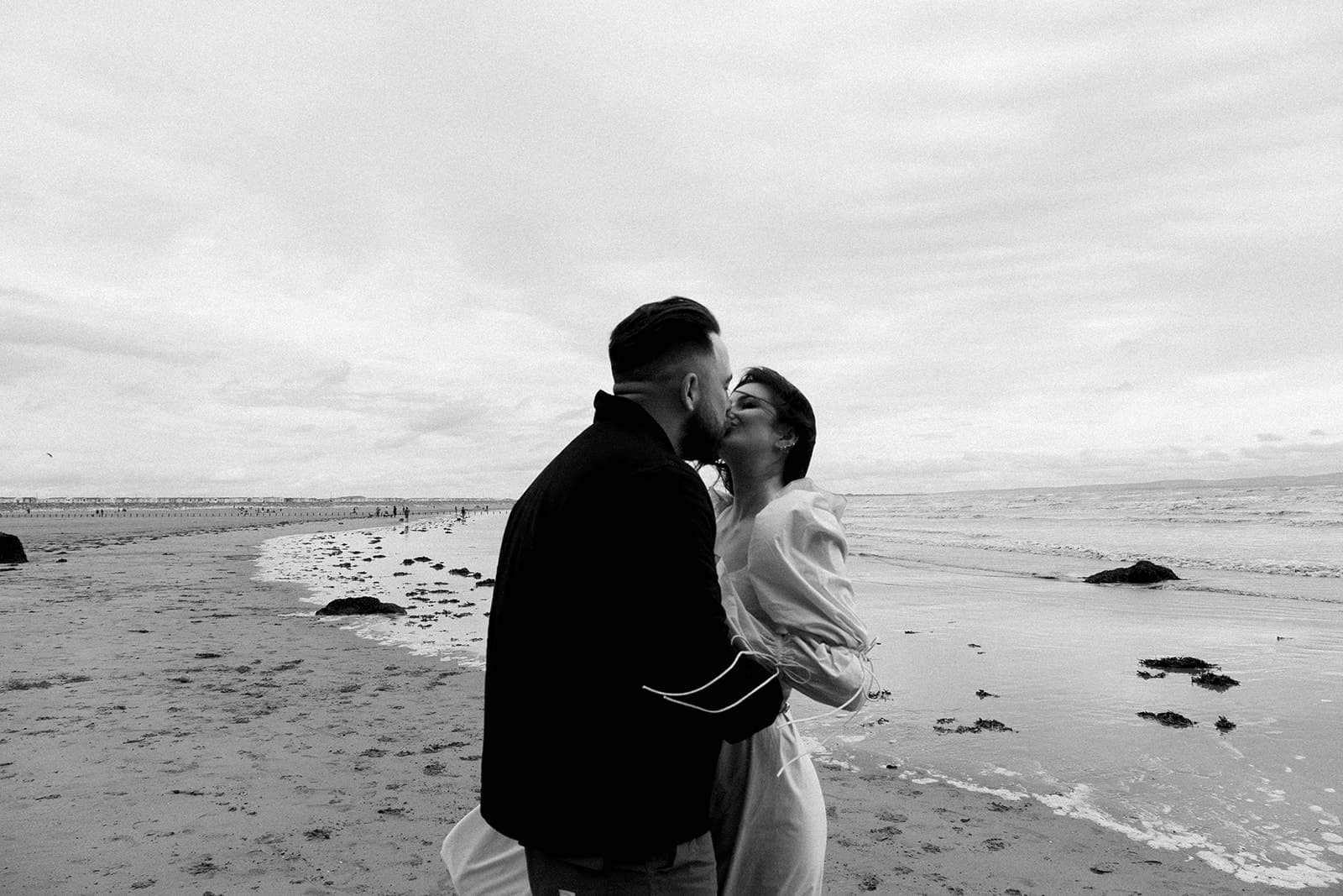 A couple embracing on a cloudy beach with gentle waves and a distant pier. brean beach