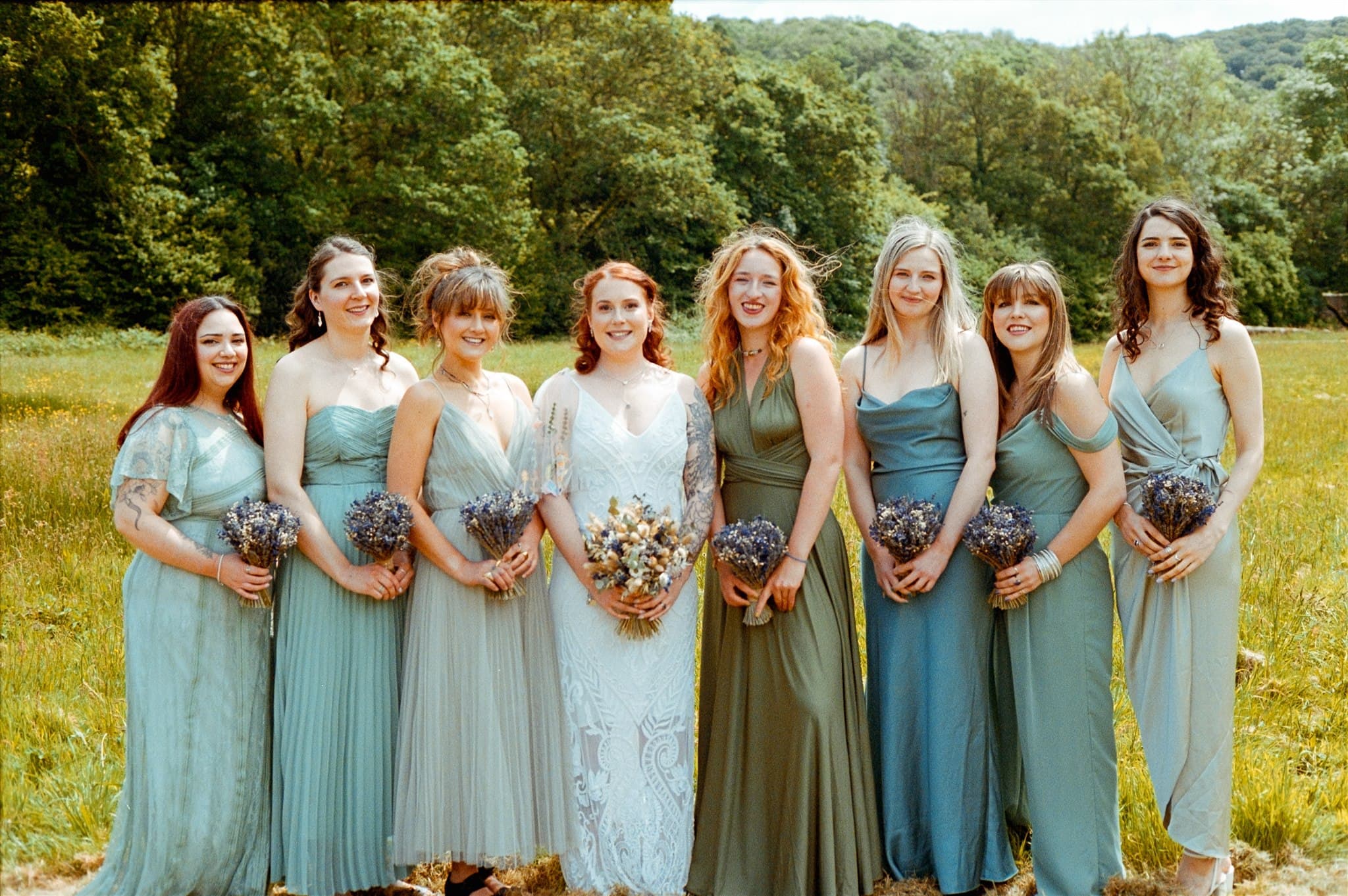 A group of bridesmaids in matching dresses holding bouquets in a field. Film Photo