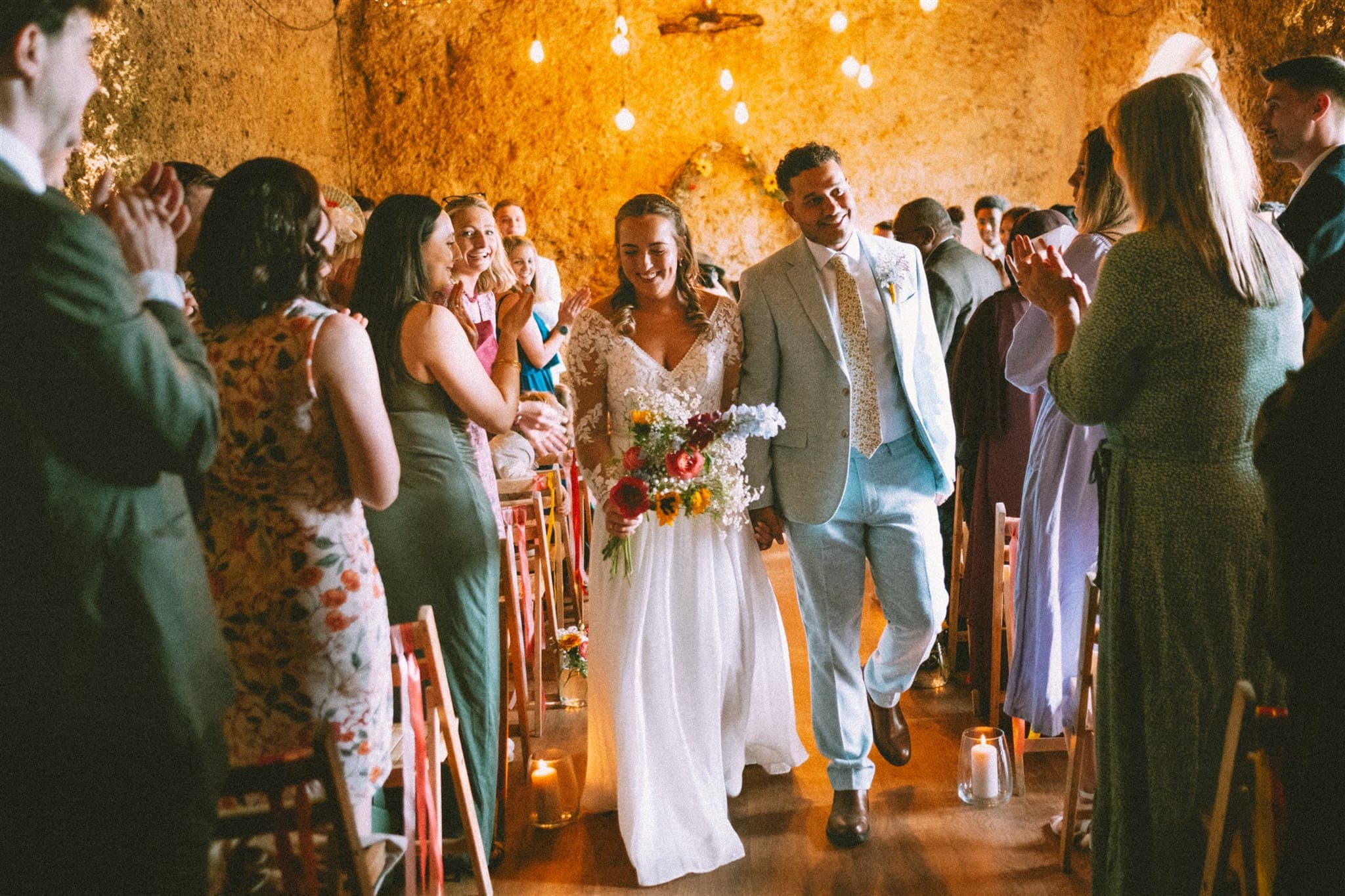 A bride and groom walk down the aisle as guests applaud.