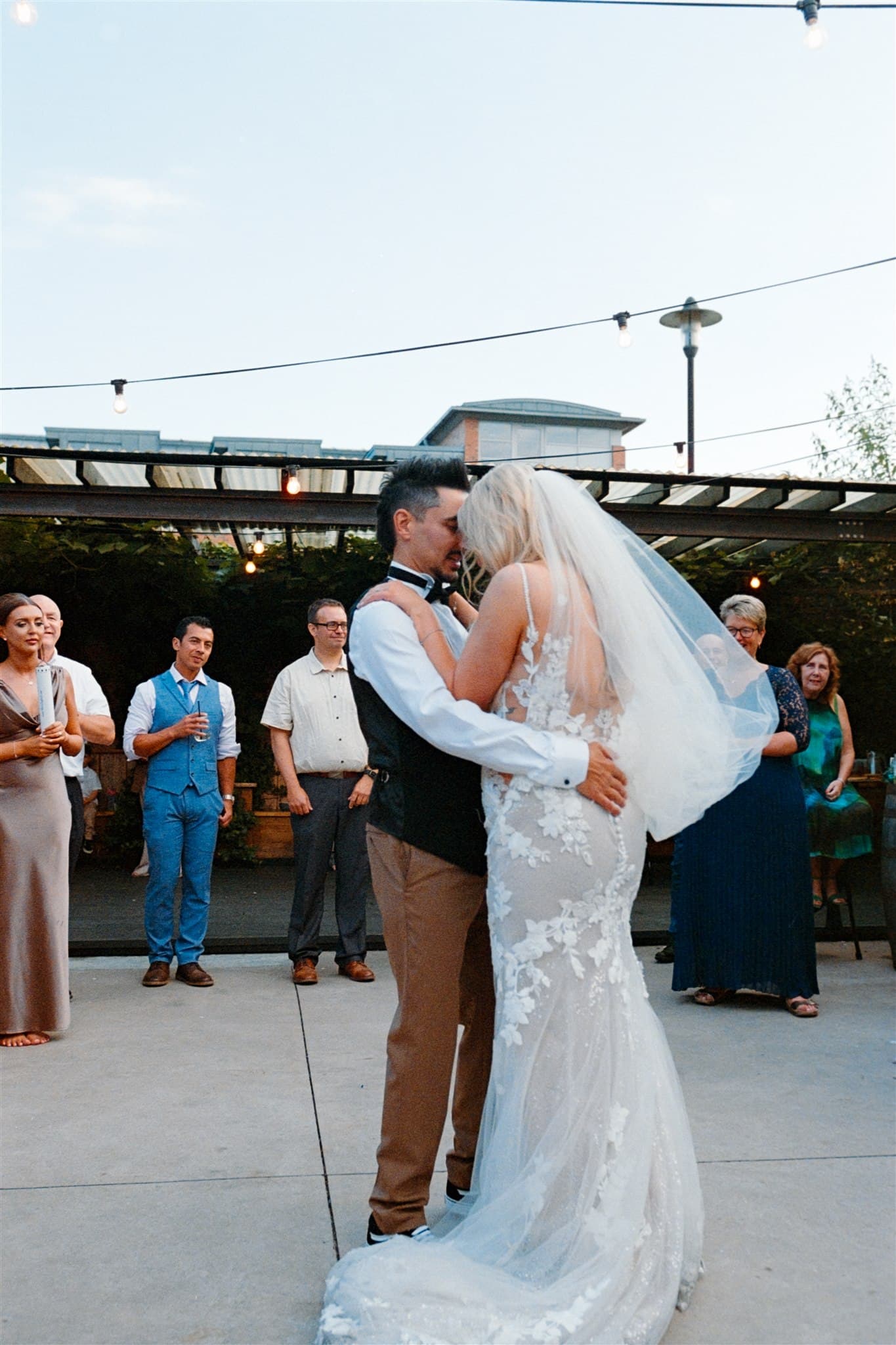 Film photo of a bride and groom dancing outdoors with guests watching.