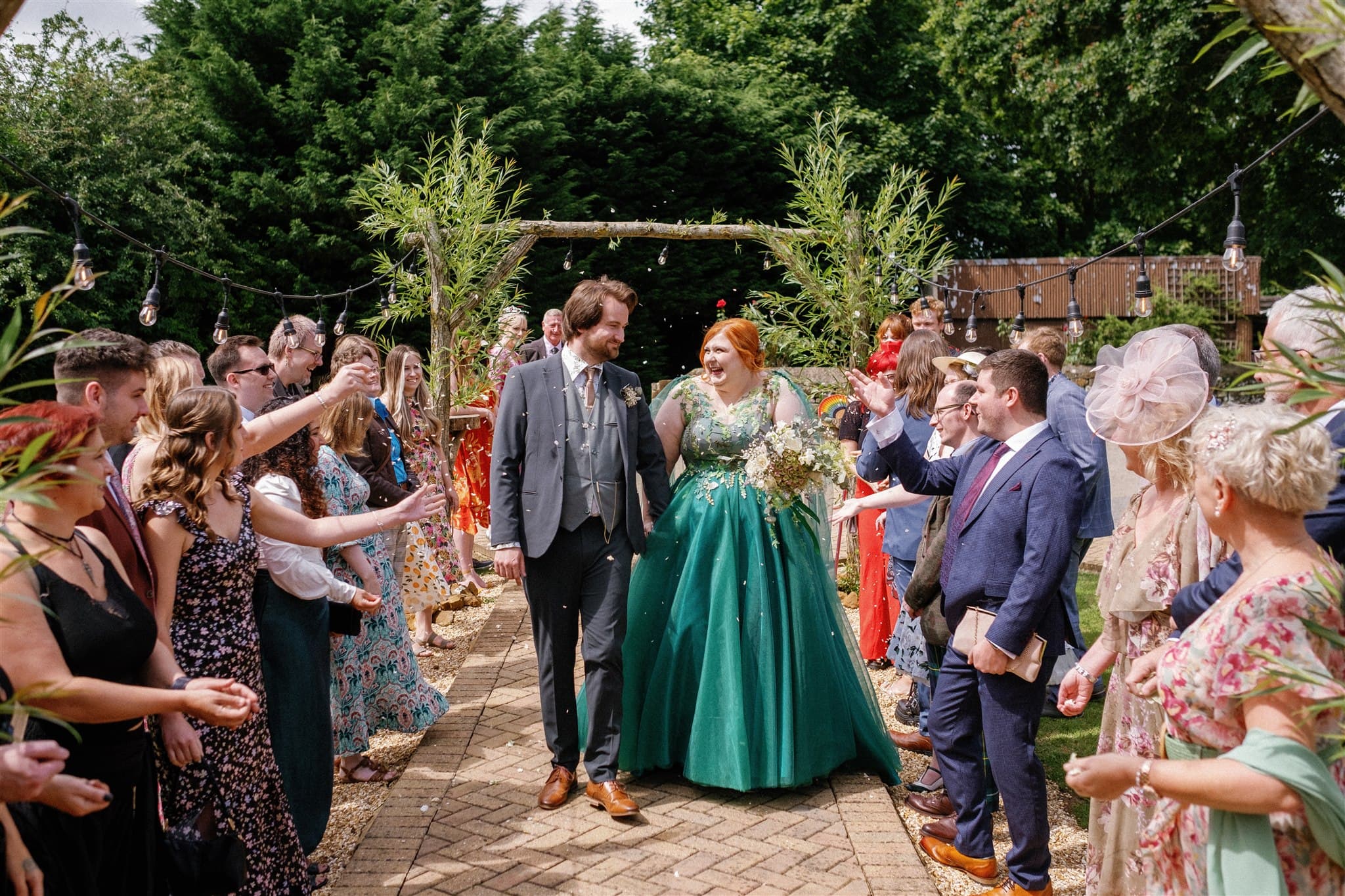 A bride in a green wedding dress and groom walk through a cheering crowd throwing confetti at wedding.