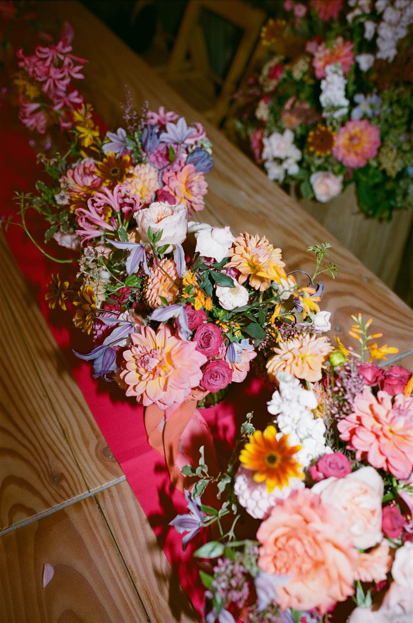A film photo of Vibrant floral arrangement on a wooden table with a pink runner.