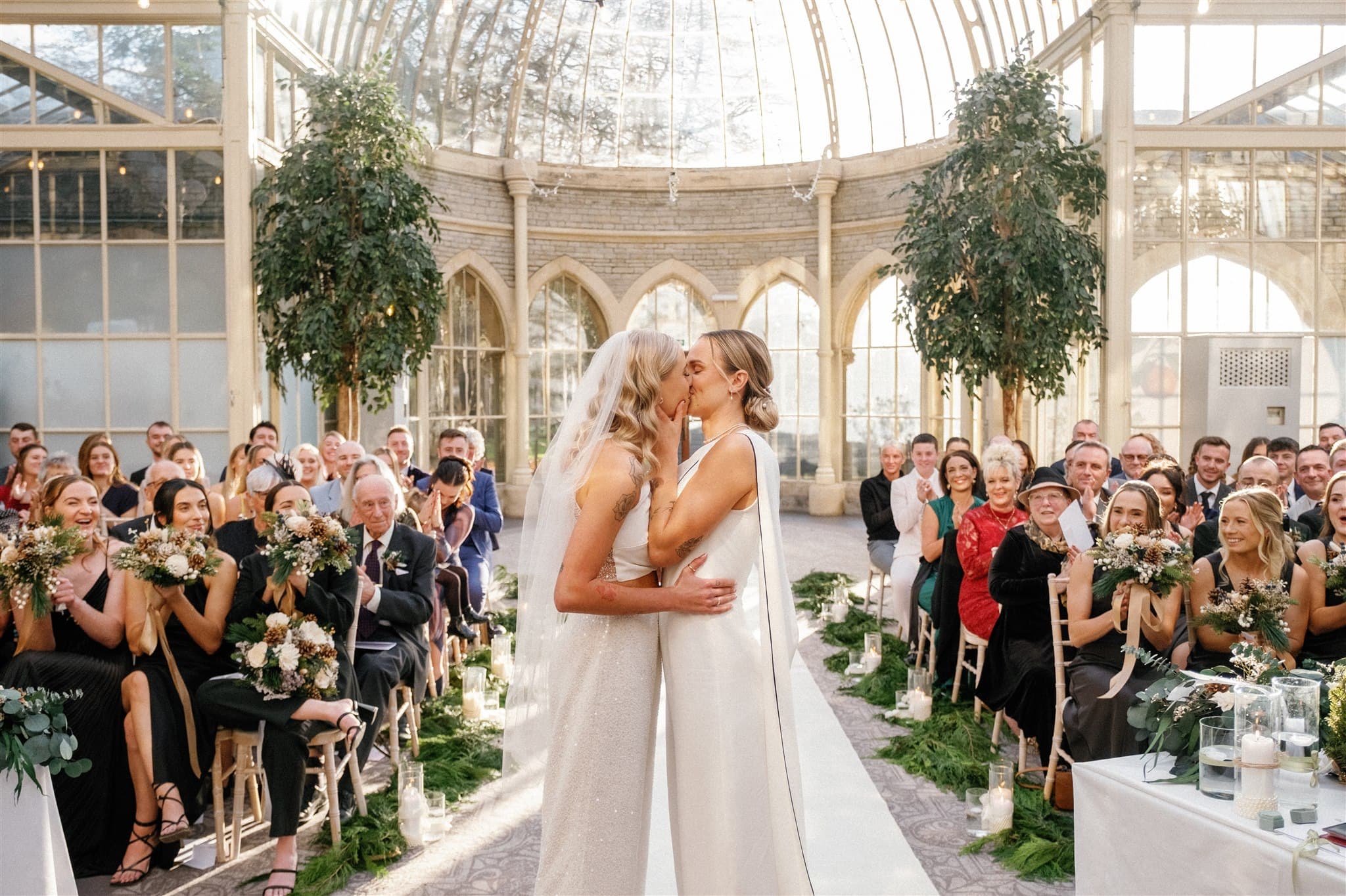 A wedding ceremony in a glasshouse with guests seated along the aisle.