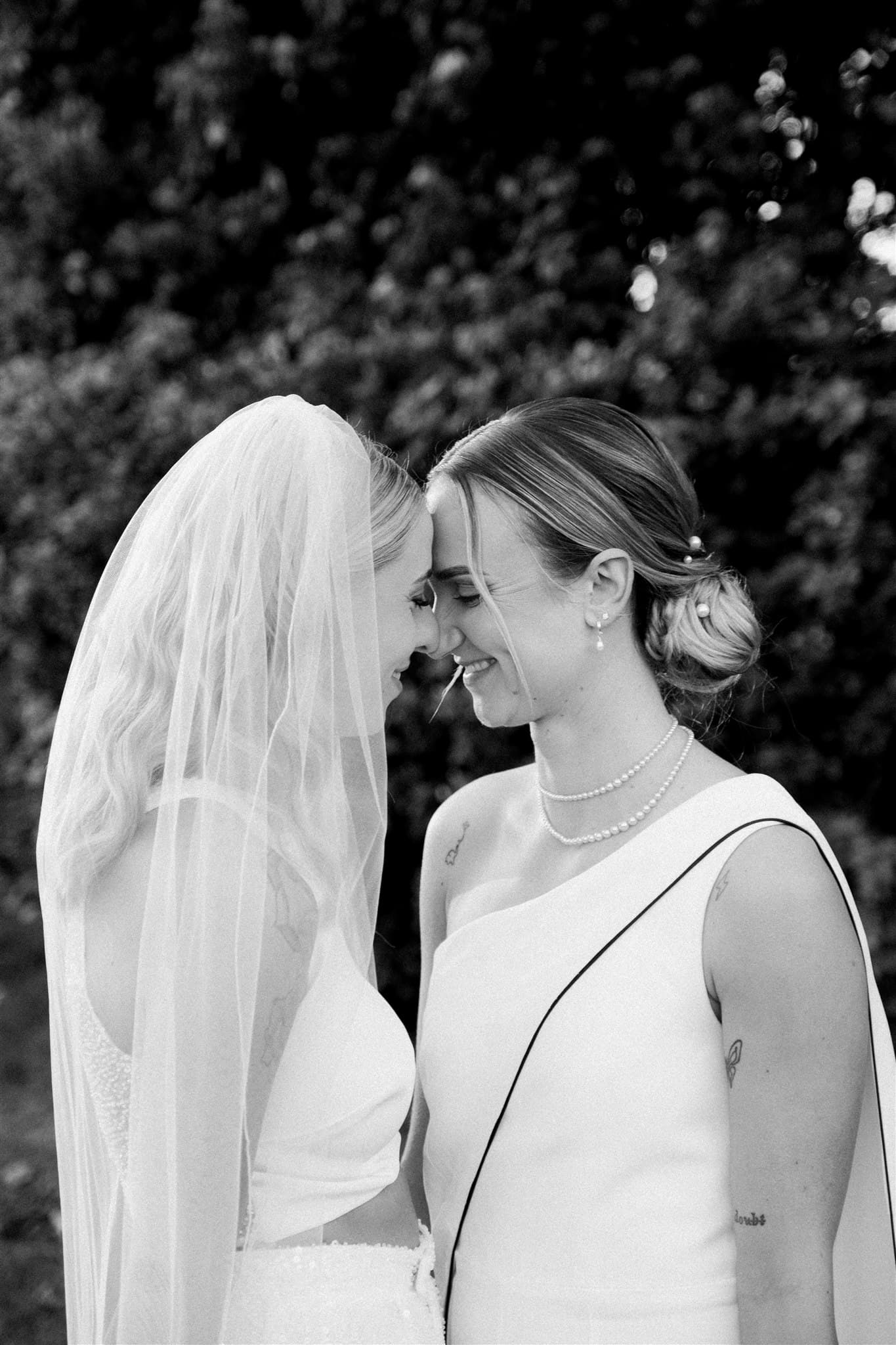 Two brides facing each other, one in a veil, in a black and white photo.