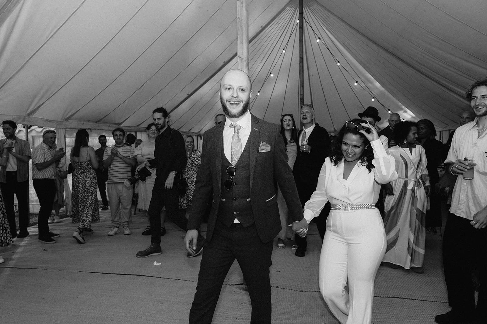 Guests in formal attire at an event inside a tent with string lights.