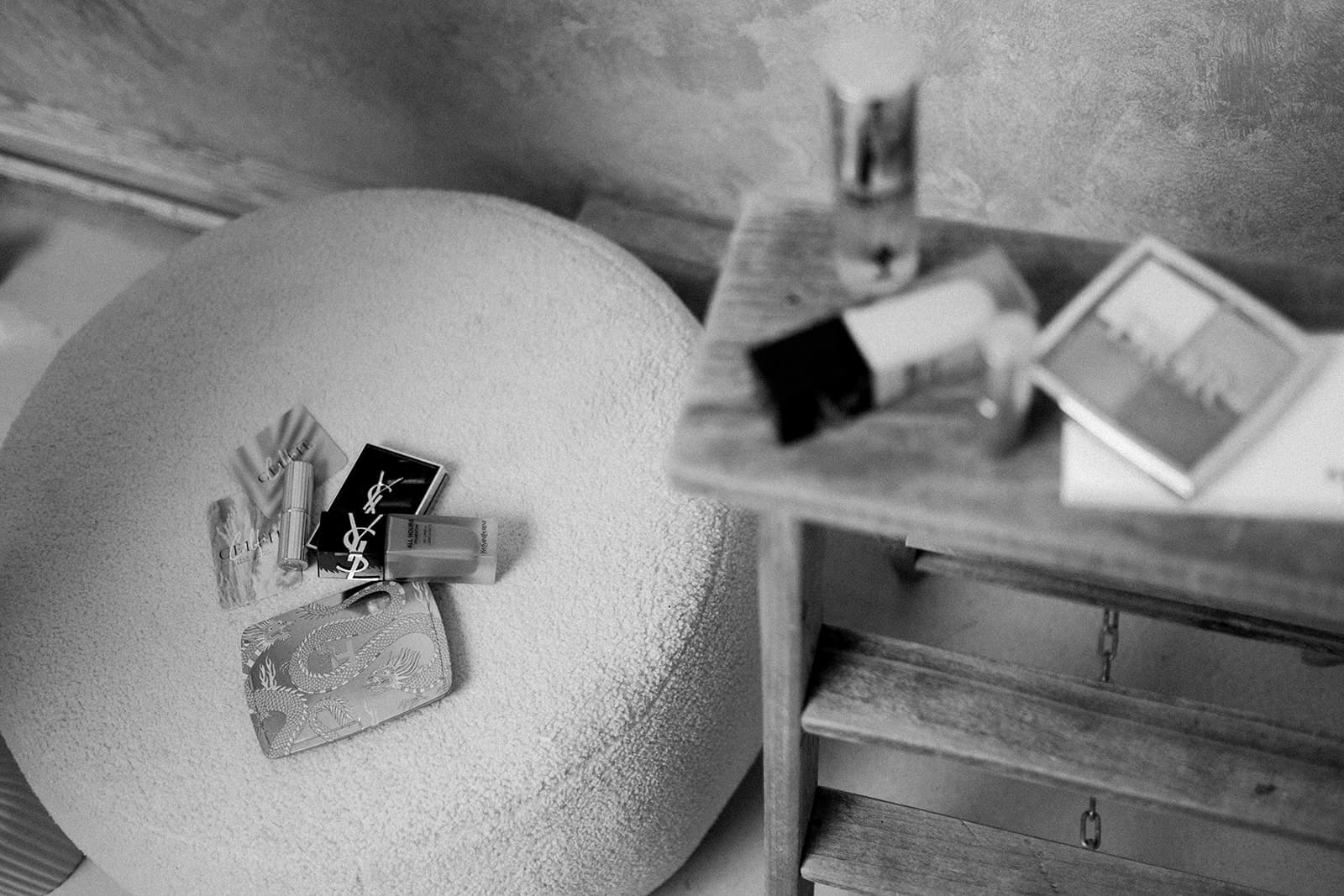 Monochrome image of makeup items and a wallet on a textured surface next to a wooden drawer.