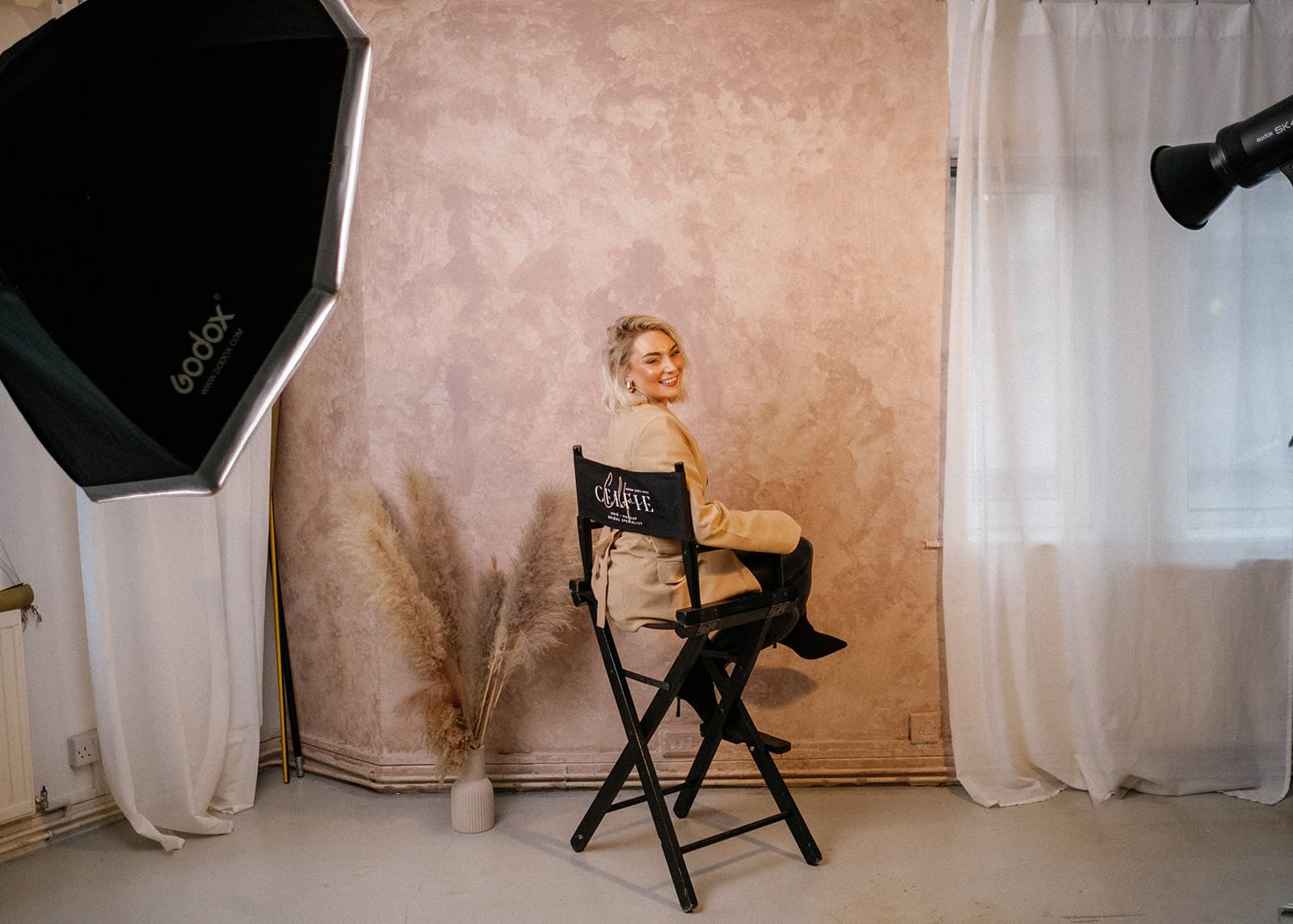 Person sitting in a director's chair in a photo studio with lighting equipment.