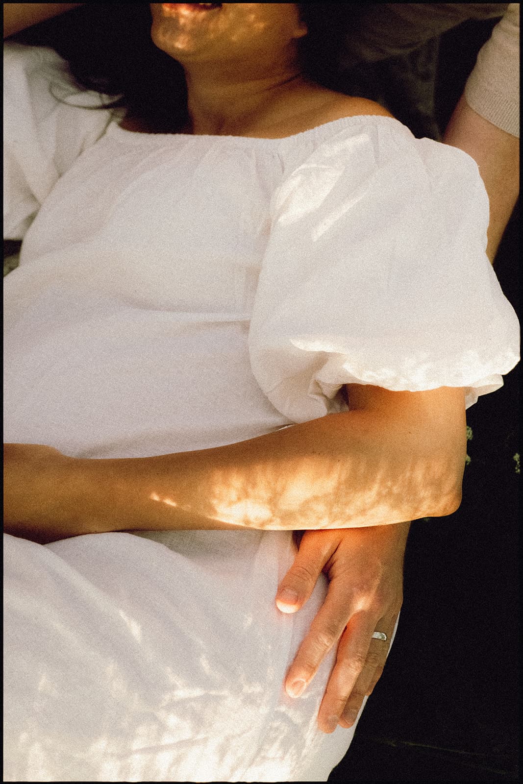 Close-up of a woman in a white puff-sleeve dress with sunlight casting patterns on her.