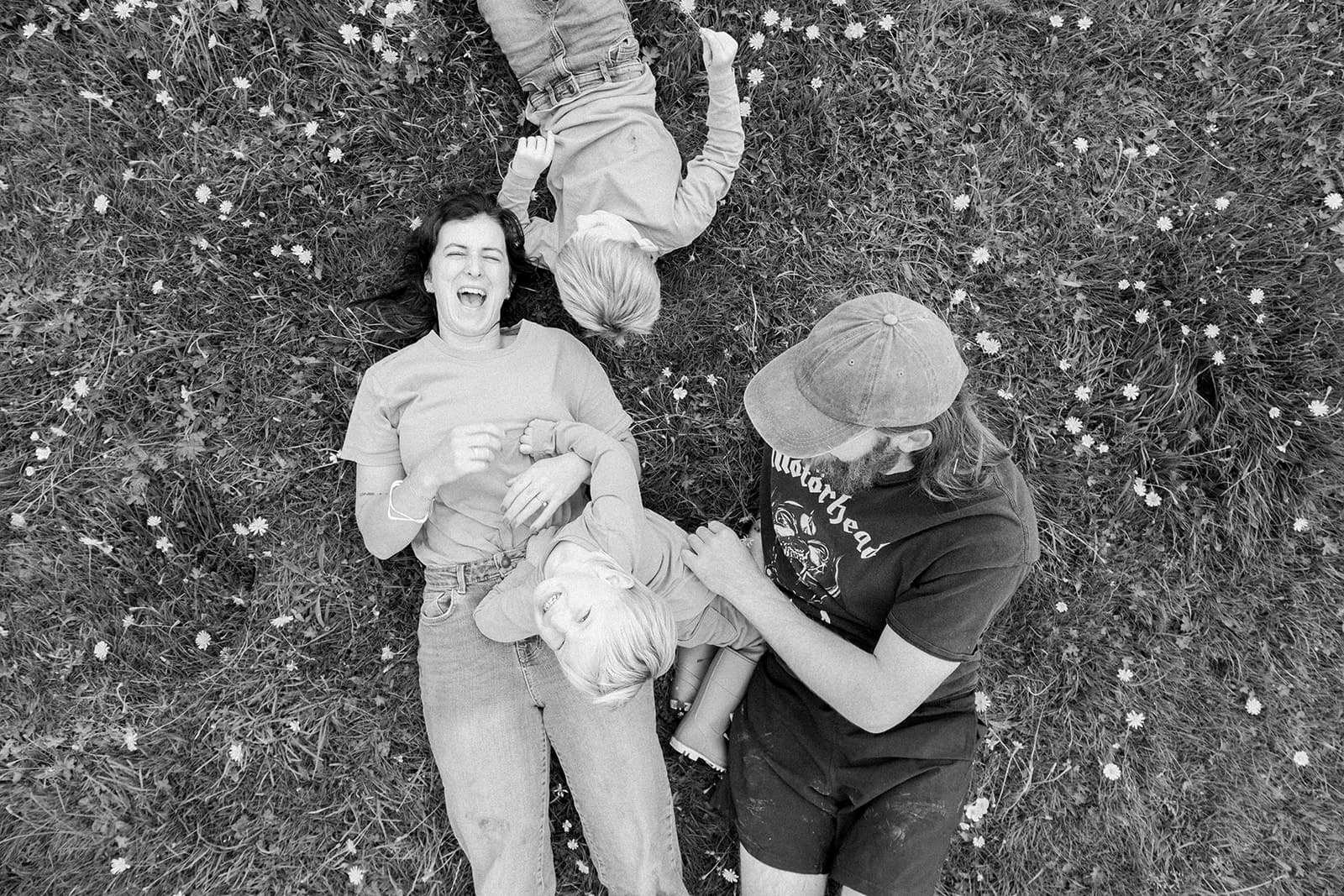 Three people lying on a grassy field with small white flowers.