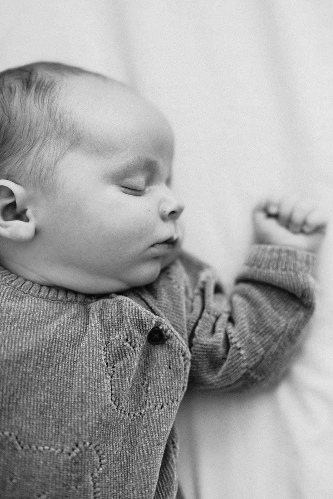 Black and white photo of a baby in a textured onesie with one arm raised.