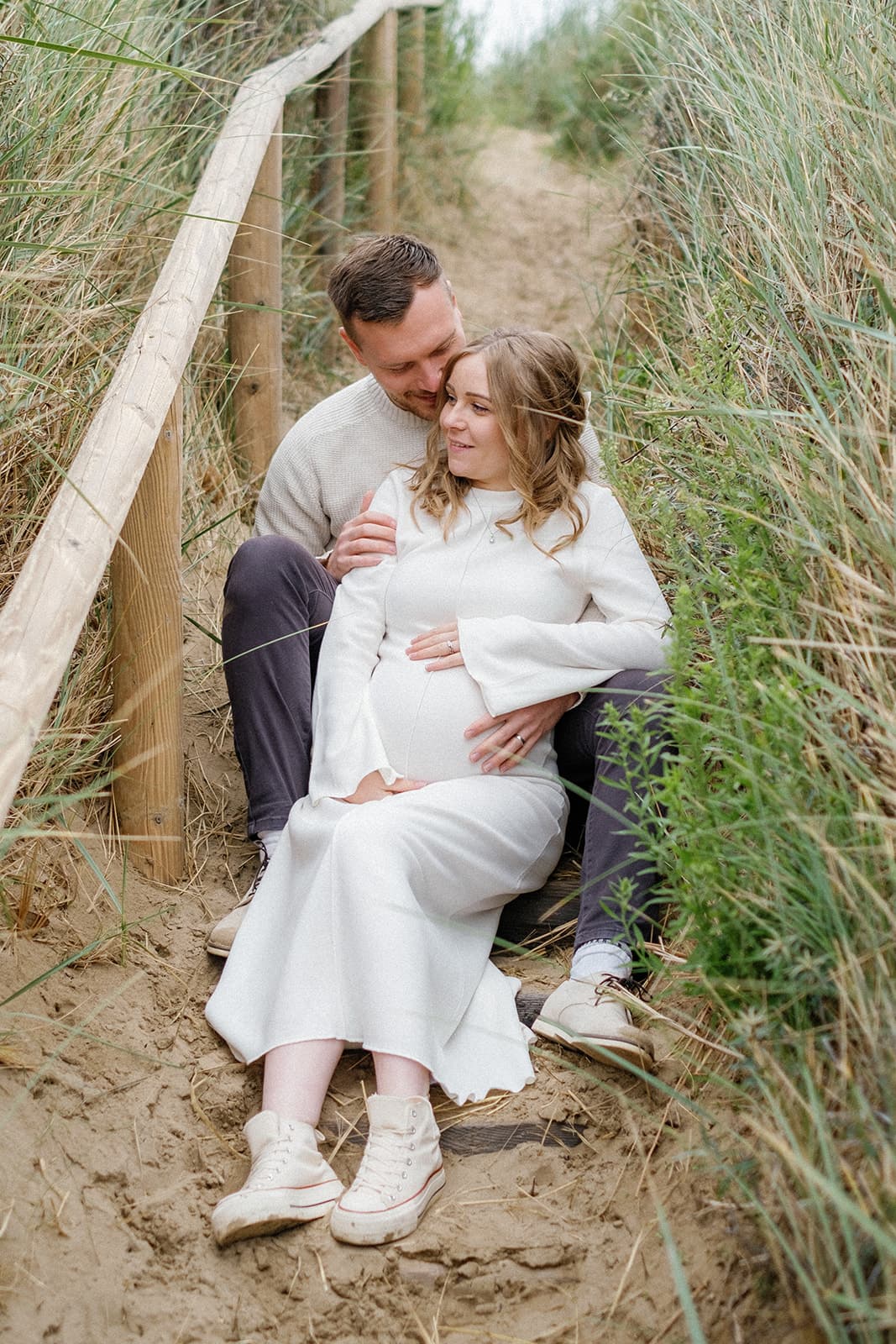 A couple sitting close together in a sandy pathway surrounded by grass.