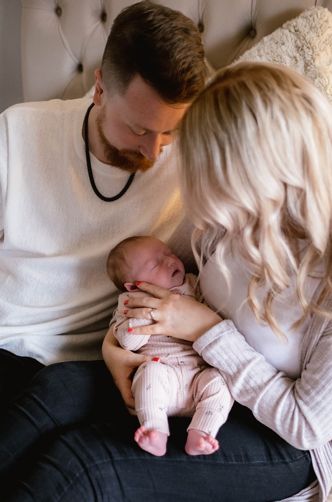Two adults holding a baby, sitting together on a couch with a cozy blanket.