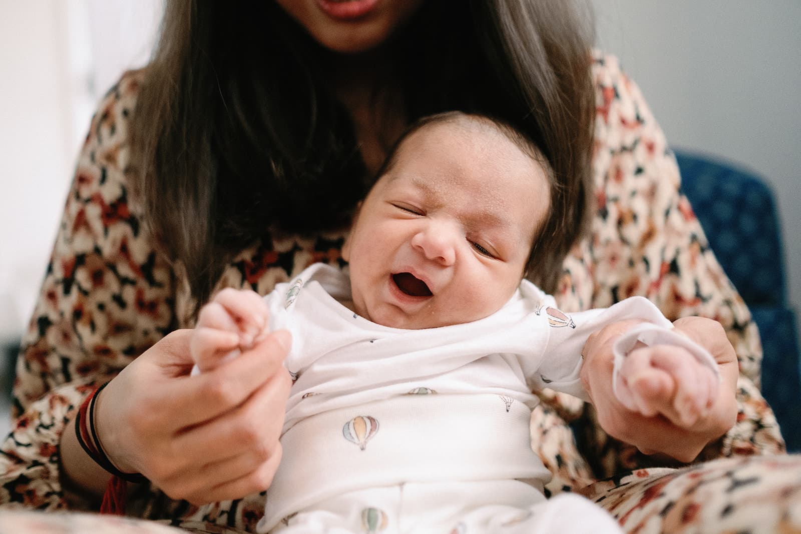 Person holding a baby's hand, wearing a patterned outfit.