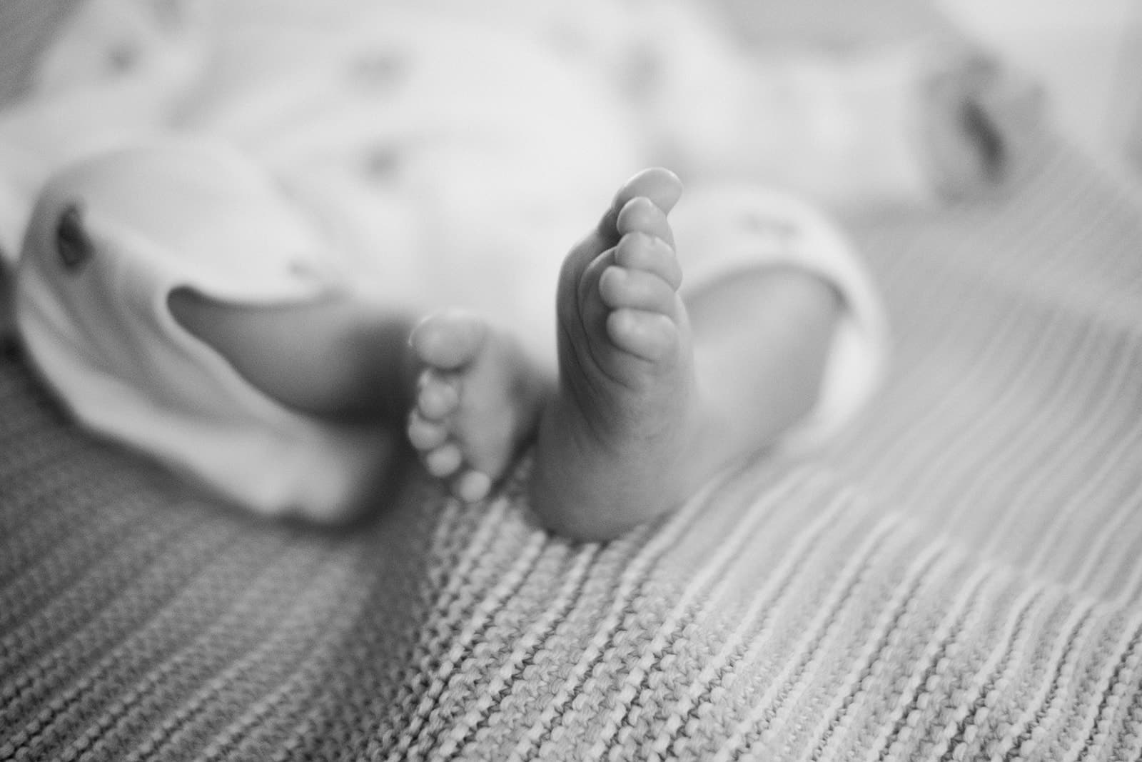 Close-up of a baby's tiny feet resting on a textured blanket, softly blurred for a gentle, tender feel in black and white.