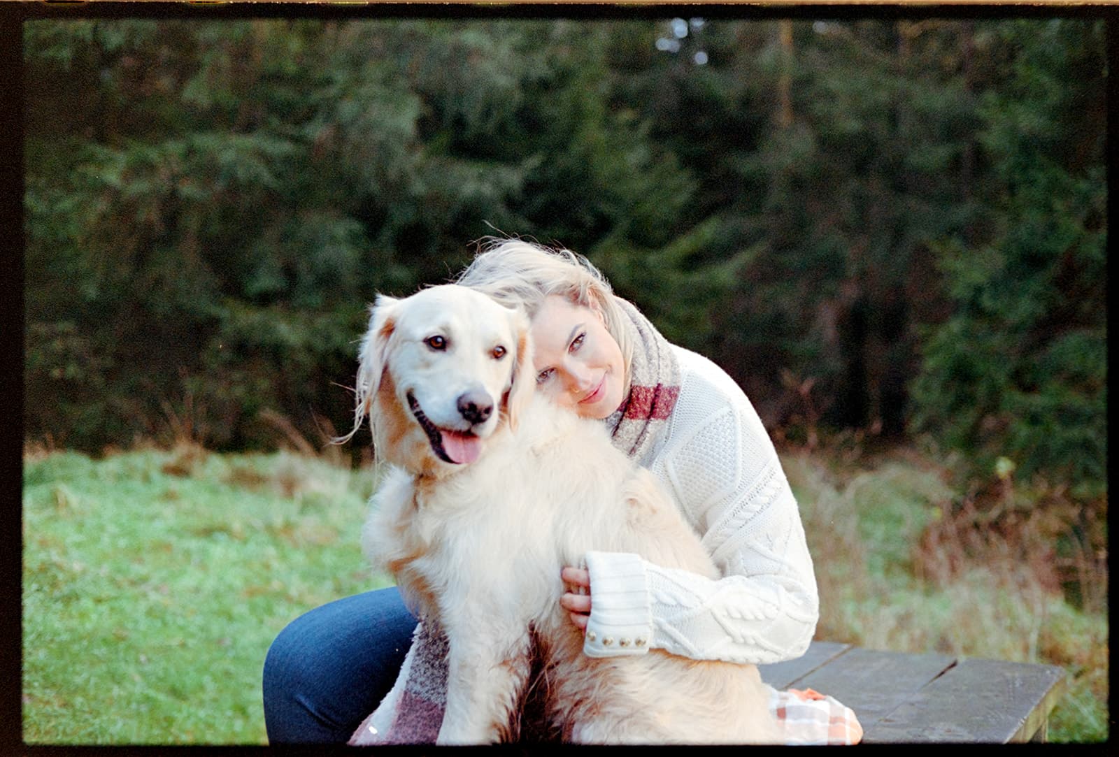 Film photo, Person in a white sweater embracing a golden retriever outdoors.