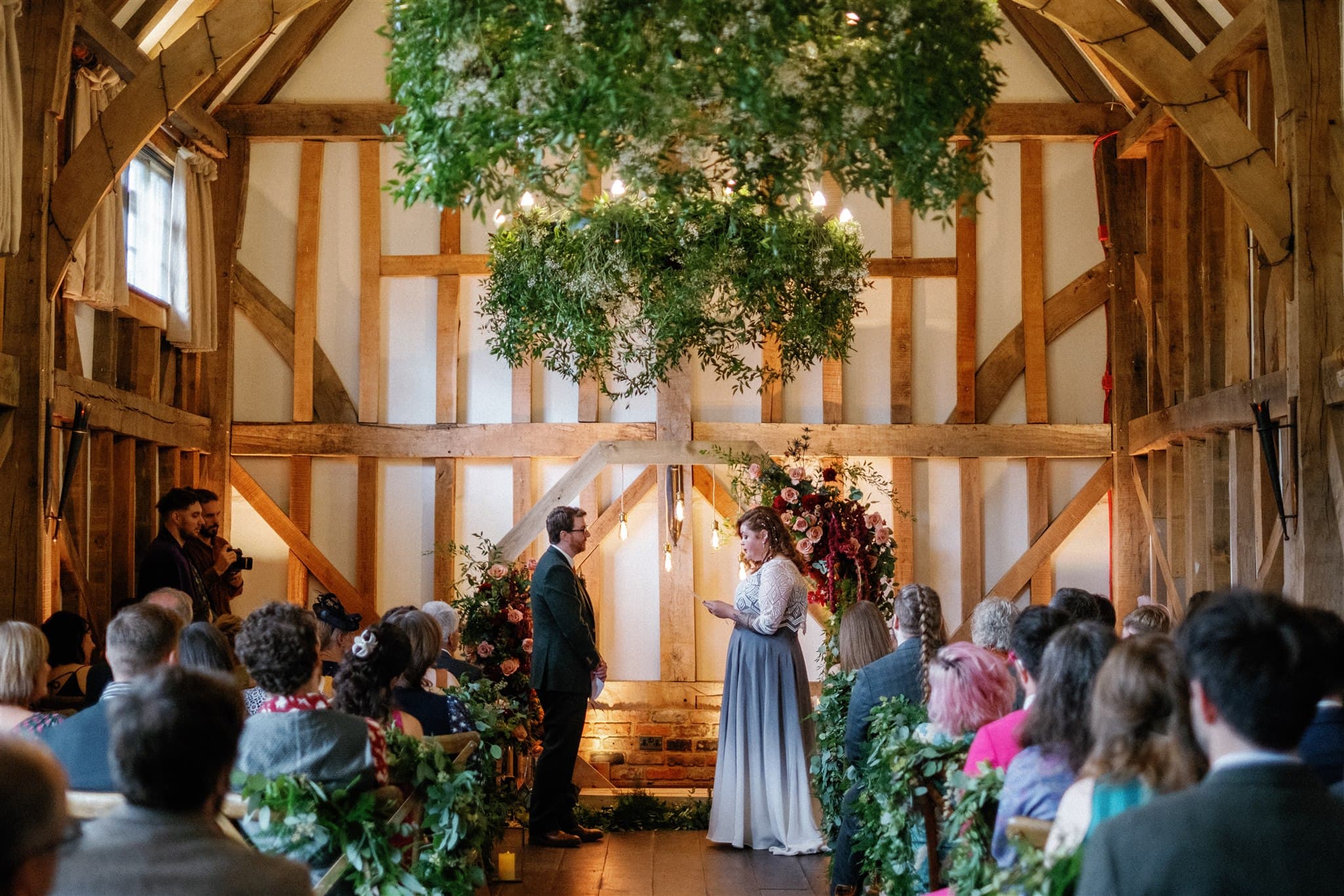 A wedding ceremony in a rustic barn decorated with lush florals and greenery.
