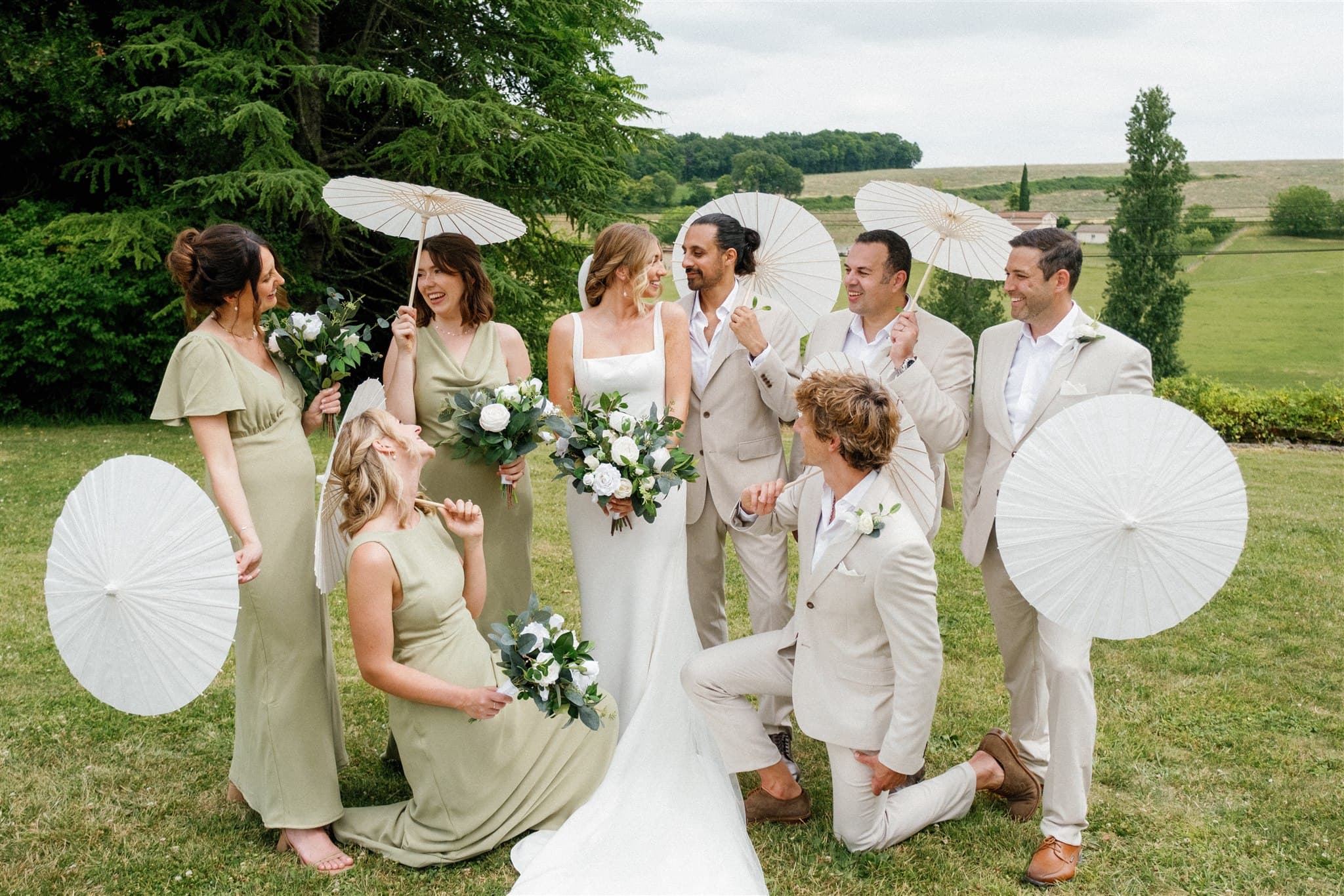 Elegant wedding set on a wooden table, featuring an invitation with a couple's photo, sage-green ribbon and envelope, small jewelry box, and perfume.
