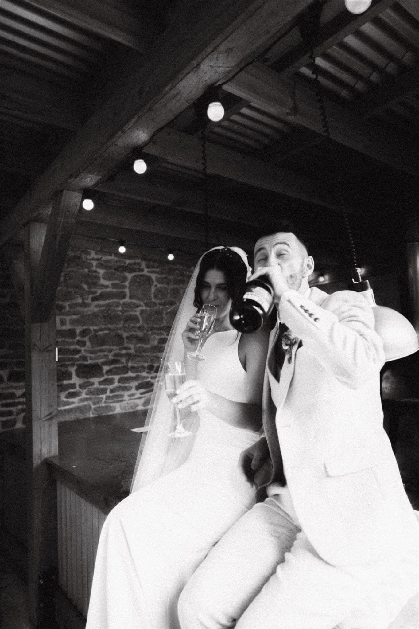 A bride and groom toasting with champagne in a rustic setting with string lights overhead.