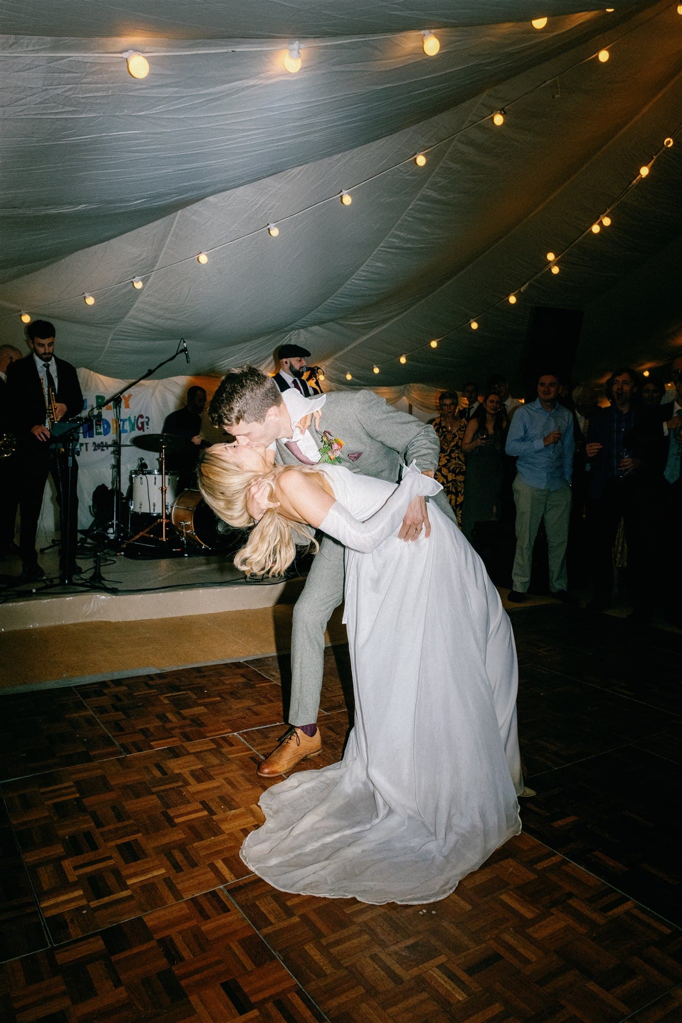 Couple dancing with a dip under string lights at a party.