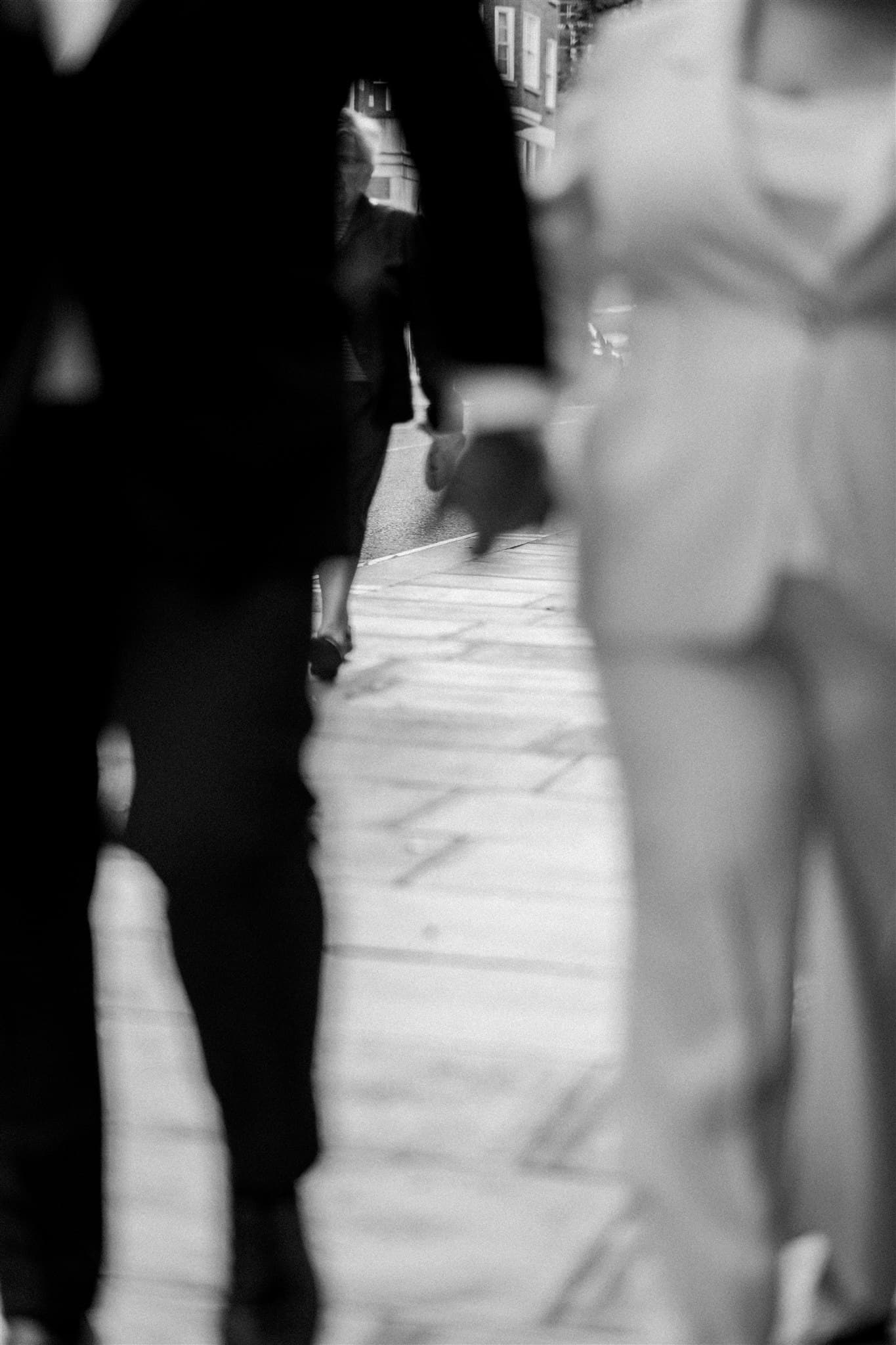 Blurry black and white photo of people walking on a sidewalk, faces not visible.