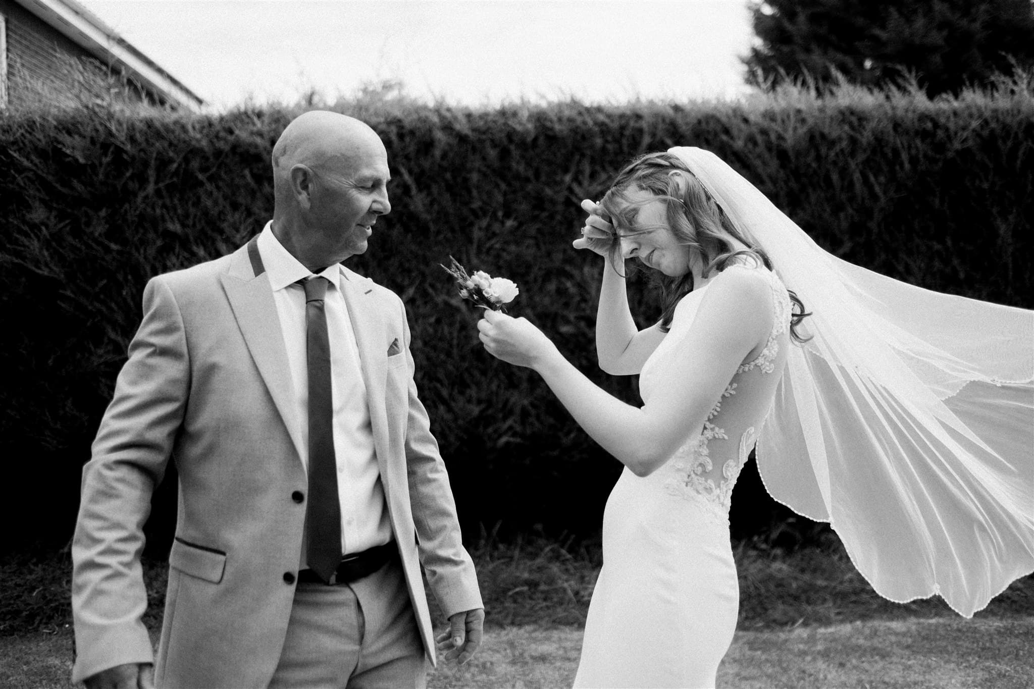 A bride in a white dress and a FOB in a suit standing outdoors, with a hedge in the background.